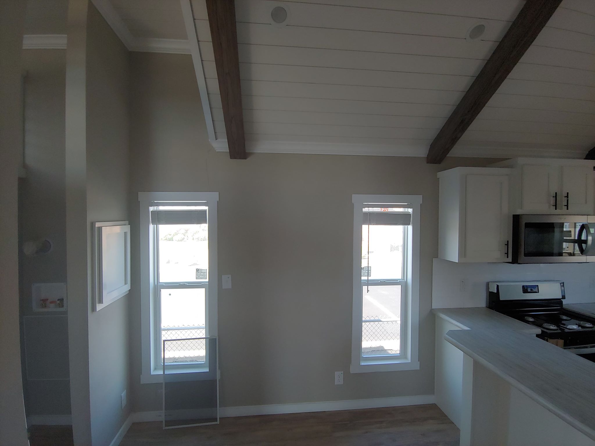 Bright interior with two narrow windows, light wood beams on a vaulted ceiling, and a modern kitchen with white cabinets and stainless steel appliances.