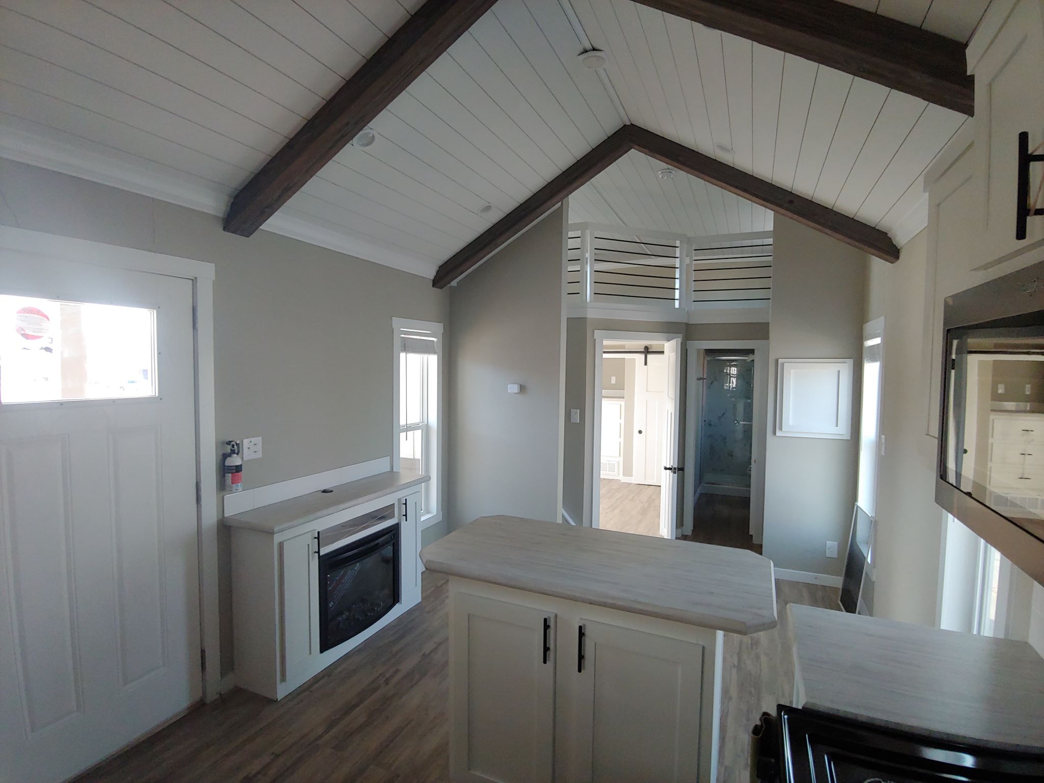 Bright, cozy interior with vaulted ceilings and rustic beams. Features a kitchen island, fireplace, wood flooring, and neutral color scheme. Peaceful ambiance.