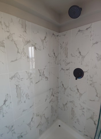 Shower with white marble-patterned tiles, dark round showerhead, and matching faucet. Clean, modern design with a calm, polished atmosphere.