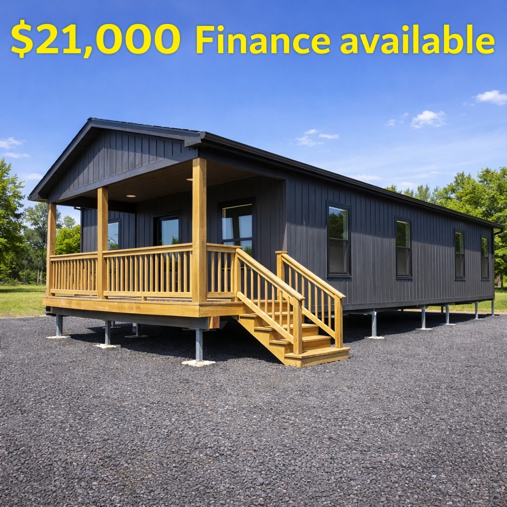 Gray modular home with a wooden porch, set on gravel. Blue sky and green trees in the background. Text reads "$21,000 Finance available."