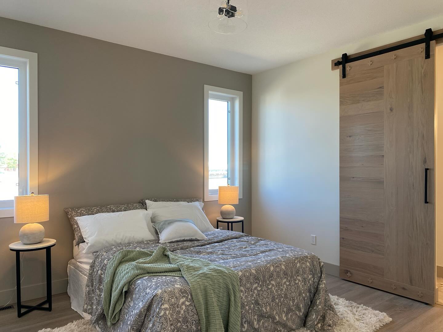 Cozy bedroom with a neatly made bed, green throw blanket, two bedside tables with lamps, and a wooden sliding door. Bright and inviting atmosphere.