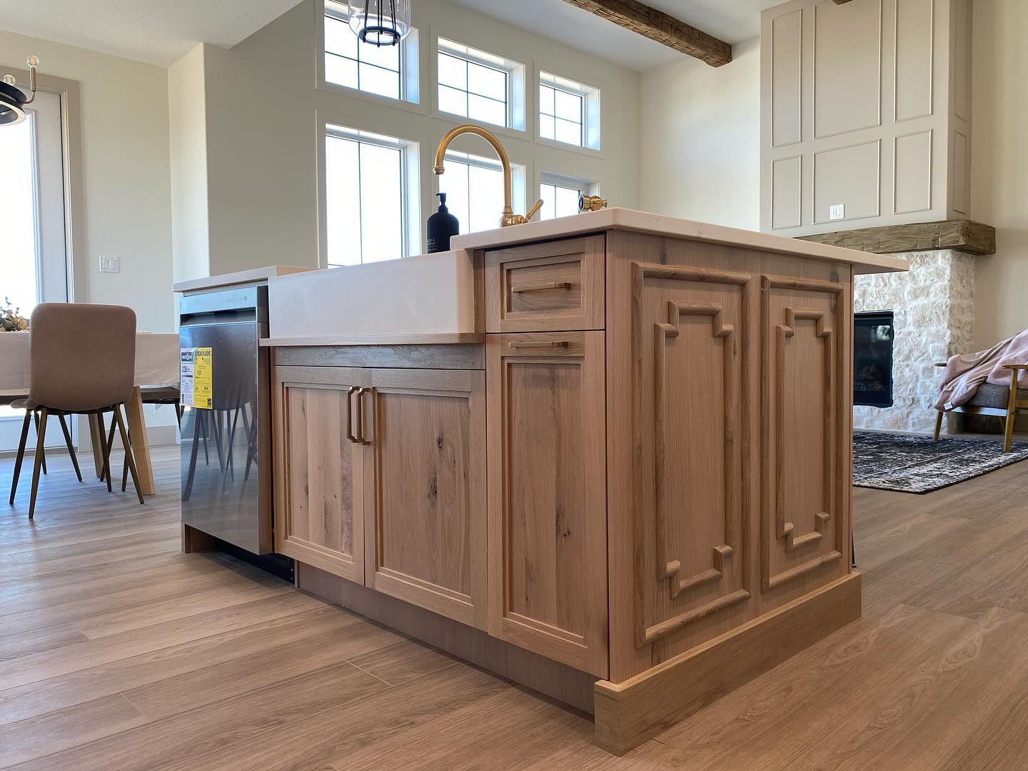 Modern kitchen interior featuring a wooden island with decorative panels, a white farmhouse sink, and a gold faucet. Bright and welcoming.