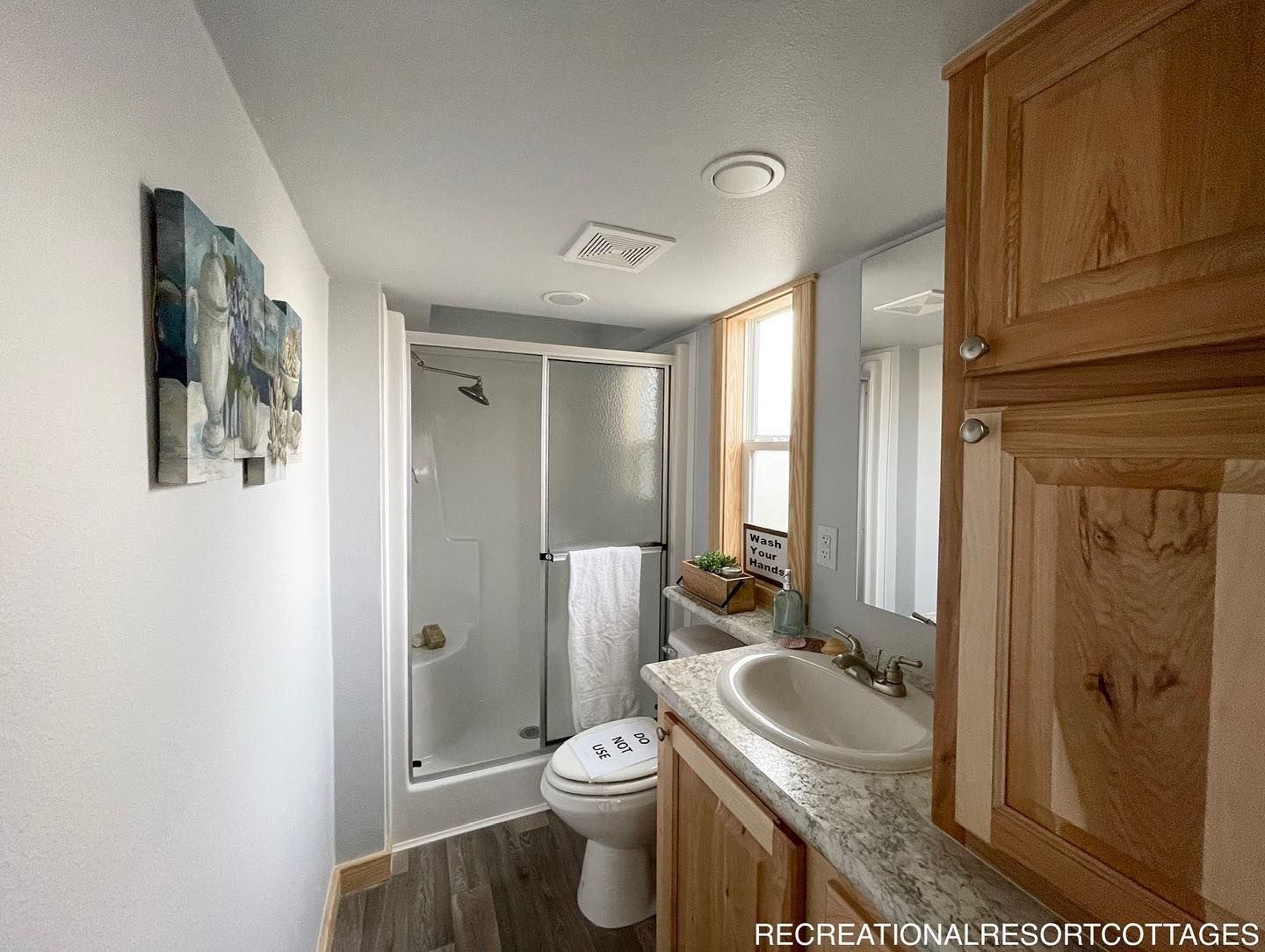 A cozy bathroom with a corner shower, frosted glass door, and a towel hanging on the rail. It features a wooden vanity with a sink, mirror, and storage above.