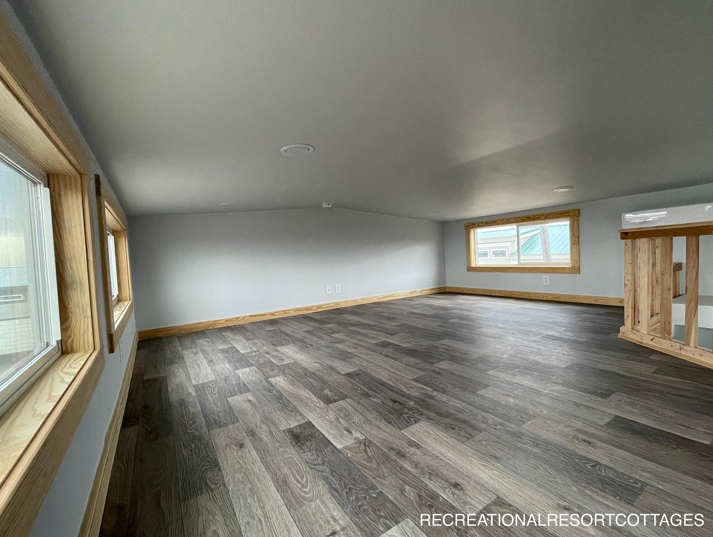 Spacious attic with gray walls, wooden trim, and dark wood floors. Sunlight streams through two rectangular windows, creating a serene ambiance.