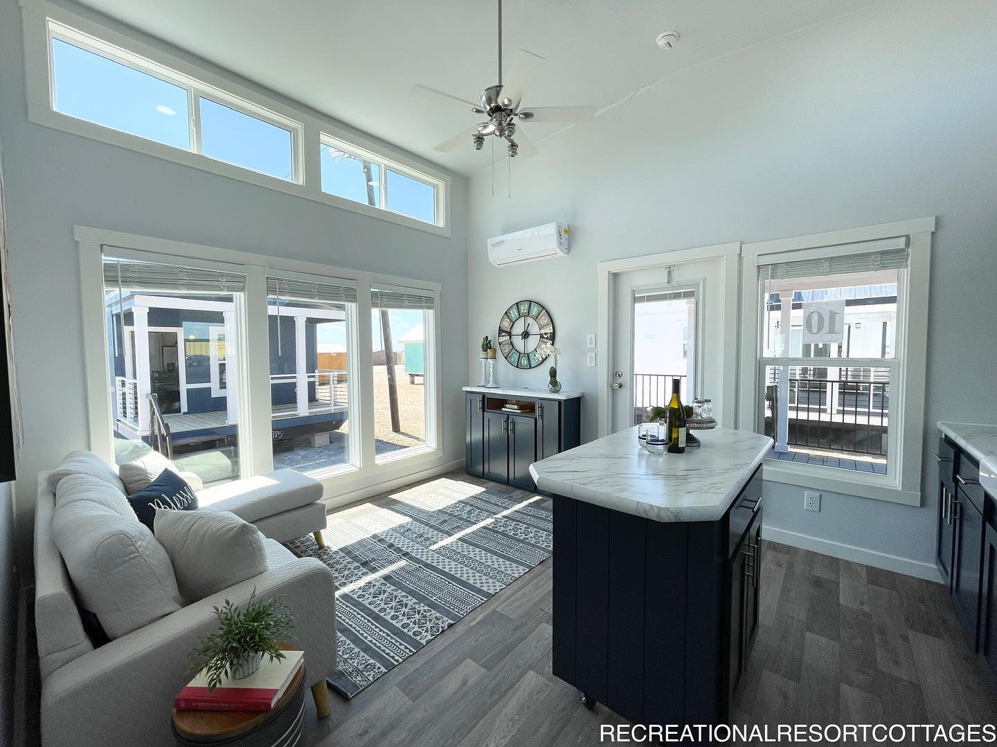 Bright, modern living area with large windows, a white couch, and navy kitchen island. Sunlight streams in, creating a cozy and inviting atmosphere.