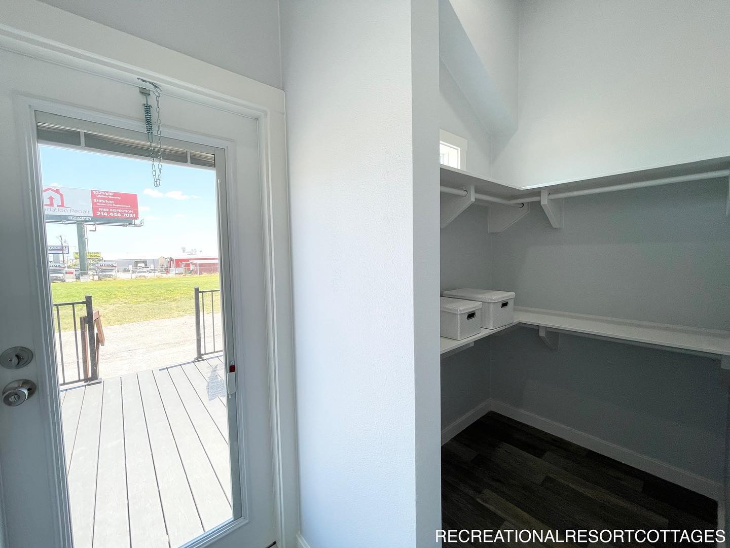 Bright, small closet with white walls and shelves. A glass door leads outside to a porch. The atmosphere is clean and minimalistic.
