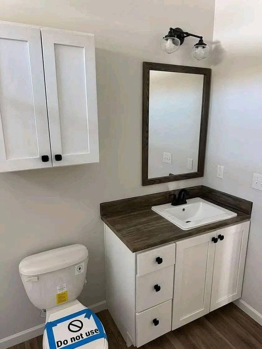 Bathroom with a white sink vanity, dark faucet, and wall-mounted mirror. A toilet with a "Do not use" sign is visible. Clean, modern design.