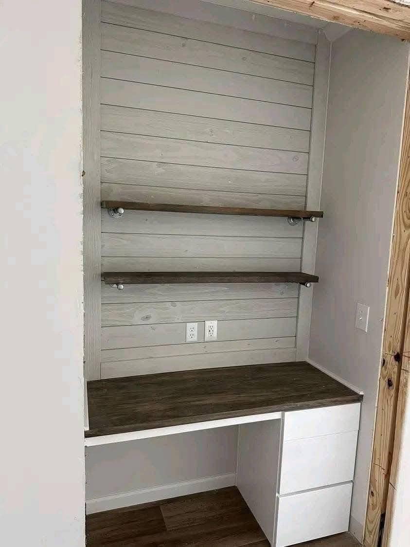 Small office nook with wooden desk, white drawers, and two floating shelves on a gray shiplap wall; minimalist and functional space.