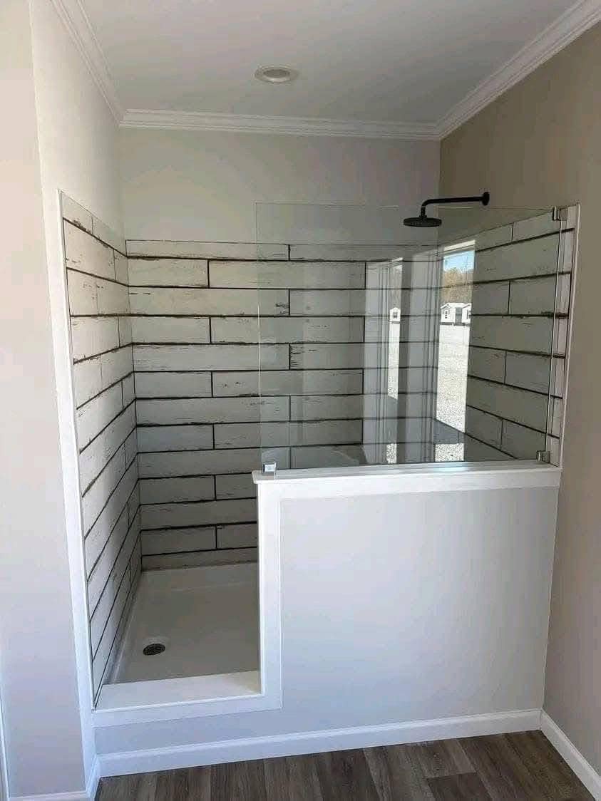 A compact, unfinished shower framed by white walls with a rustic, whitewash-style brick interior. The partially enclosed design is modern and minimalistic.