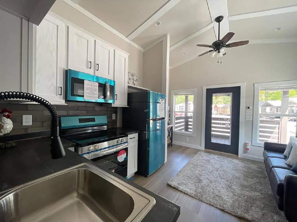 Contemporary kitchen and living area in a small home. Blue appliances, white cabinets, ceiling fan, and cozy sofa create a modern, inviting space.