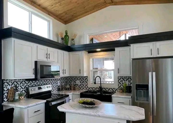 Modern kitchen with white cabinets, black hardware, and marble countertops. Stylish patterned backsplash and stainless steel appliances. Cozy and inviting atmosphere.