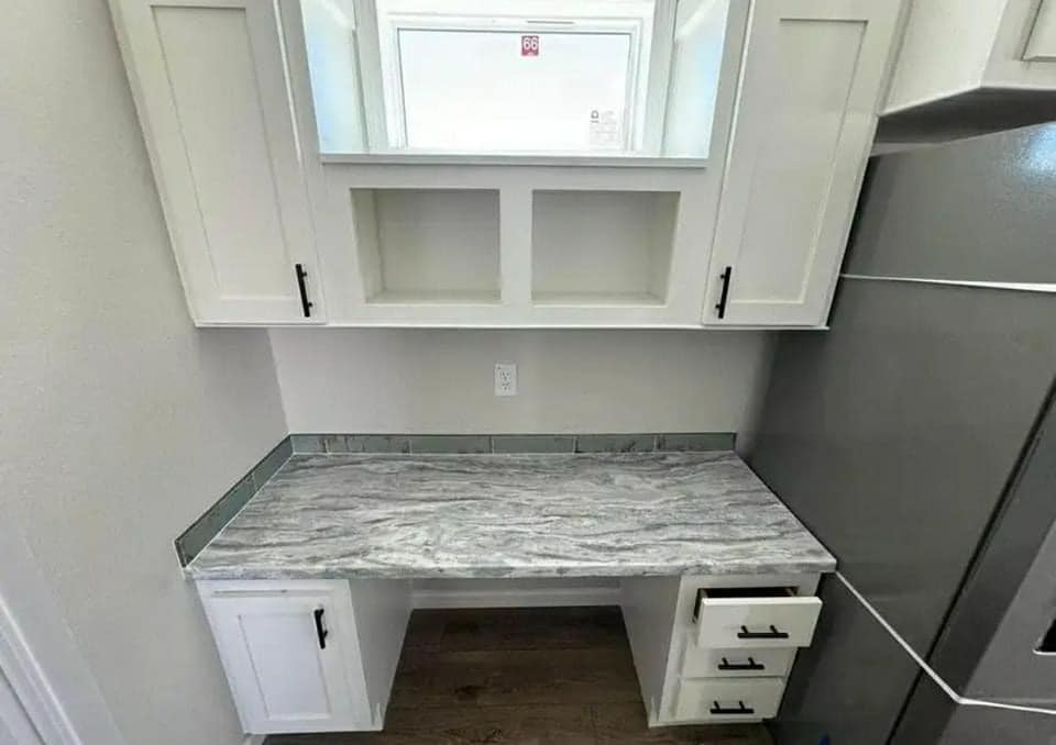 A compact laundry area with white cabinets above, a gray marble countertop below, surrounded by a washing machine on the right, conveying a clean, organized space.