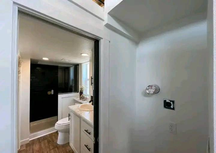 Modern bathroom with wood flooring and white fixtures. Includes a white toilet, sink with vanity, black wall accents, and ambient lighting.