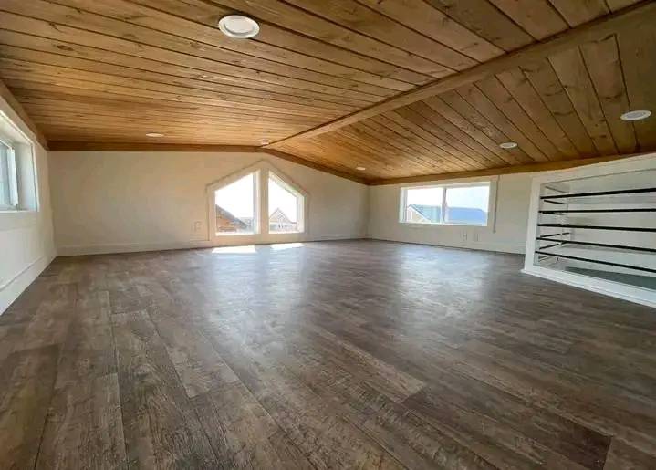 Spacious attic with wooden ceiling and floor, featuring triangular and rectangular windows providing natural light. Calm, airy atmosphere.