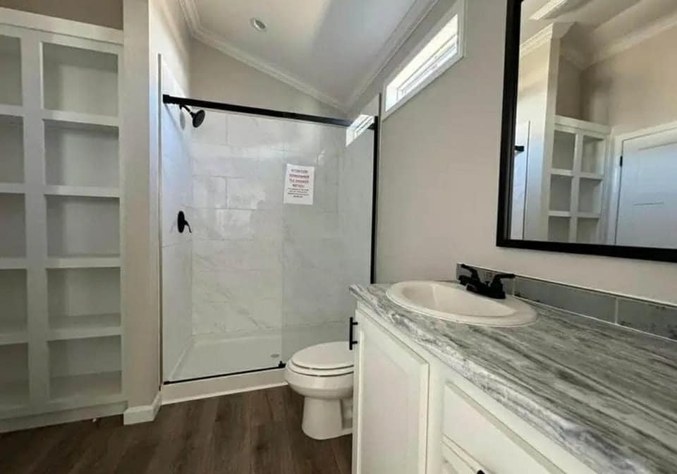 Modern bathroom with wooden floor, white marble shower, and a vanity with a granite countertop. Natural light and open shelving create an airy feel.