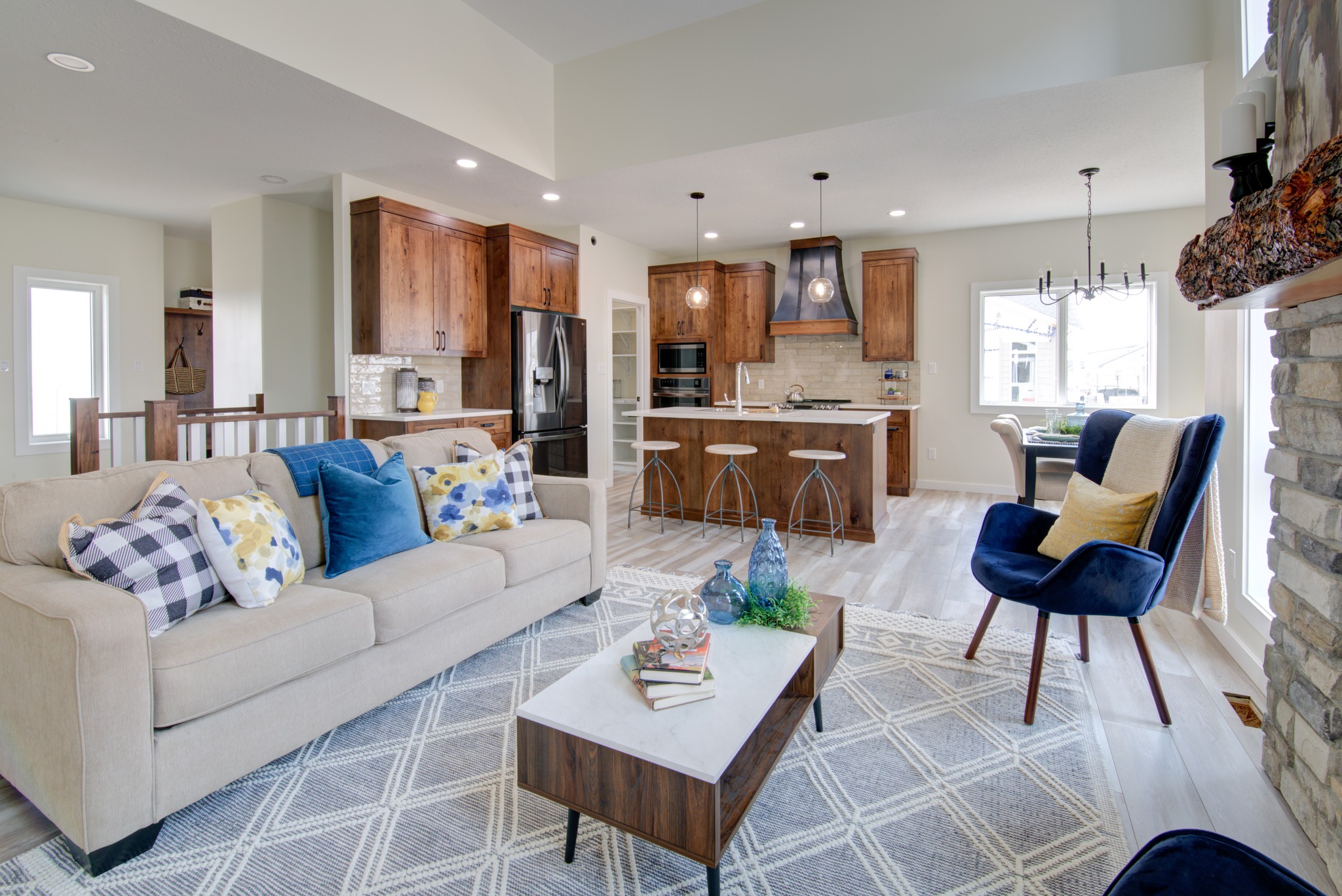Modern open-plan living room and kitchen with cozy beige sofa, colorful cushions, wooden cabinets, sleek kitchen island, and warm natural light.