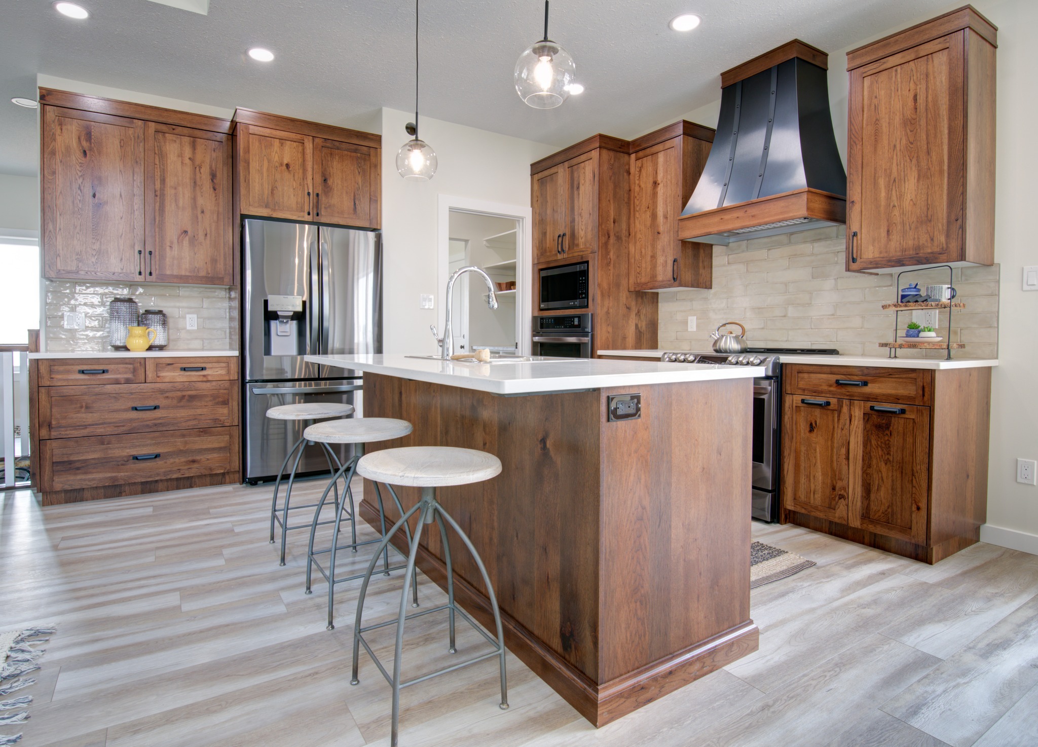 Modern kitchen with wooden cabinets, white countertops, and light wood flooring. Includes stainless steel appliances, island with stools, and pendant lights.
