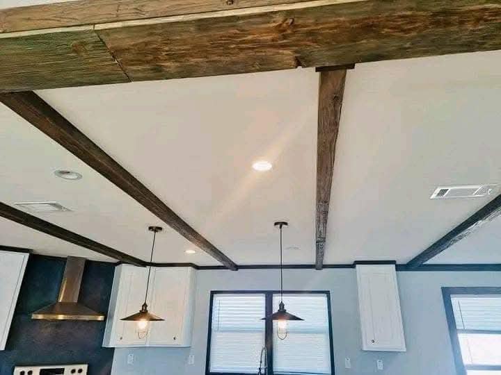 Ceiling with rustic wooden beams and two hanging pendant lights in a kitchen. White walls and cabinets are visible, creating a cozy atmosphere.