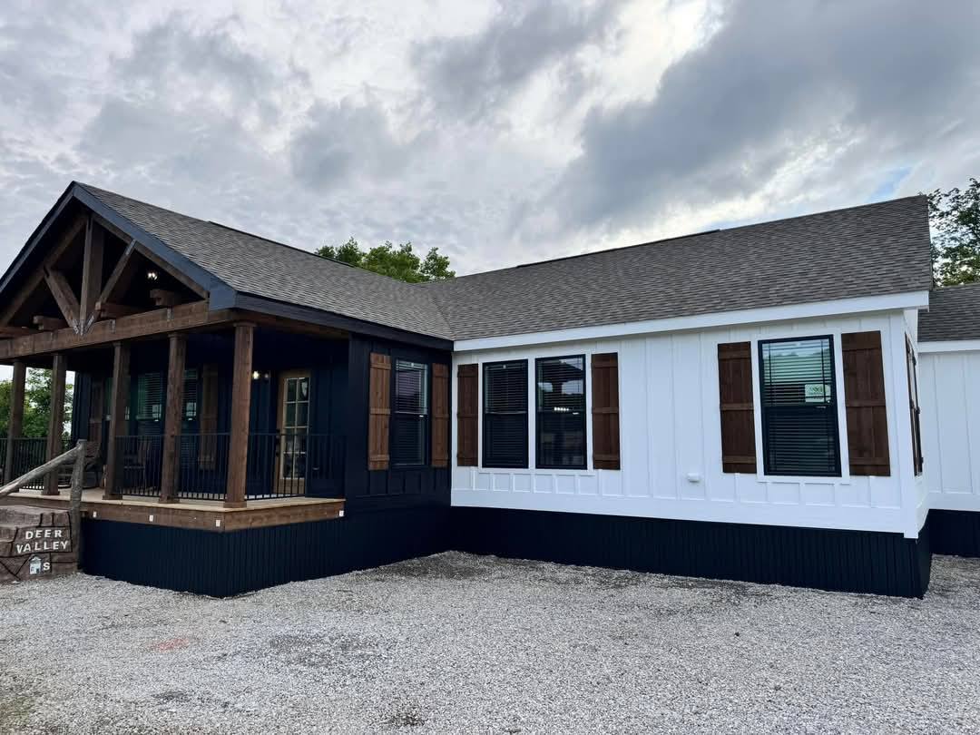 Single-story, two-tone house with black and white siding. Wood accents and a porch with a railing. Overcast sky adds a moody atmosphere.