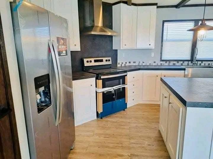 Modern kitchen with white cabinets, stainless steel appliances, and a range hood. Features tiled backsplash, wood flooring, and pendant lighting.