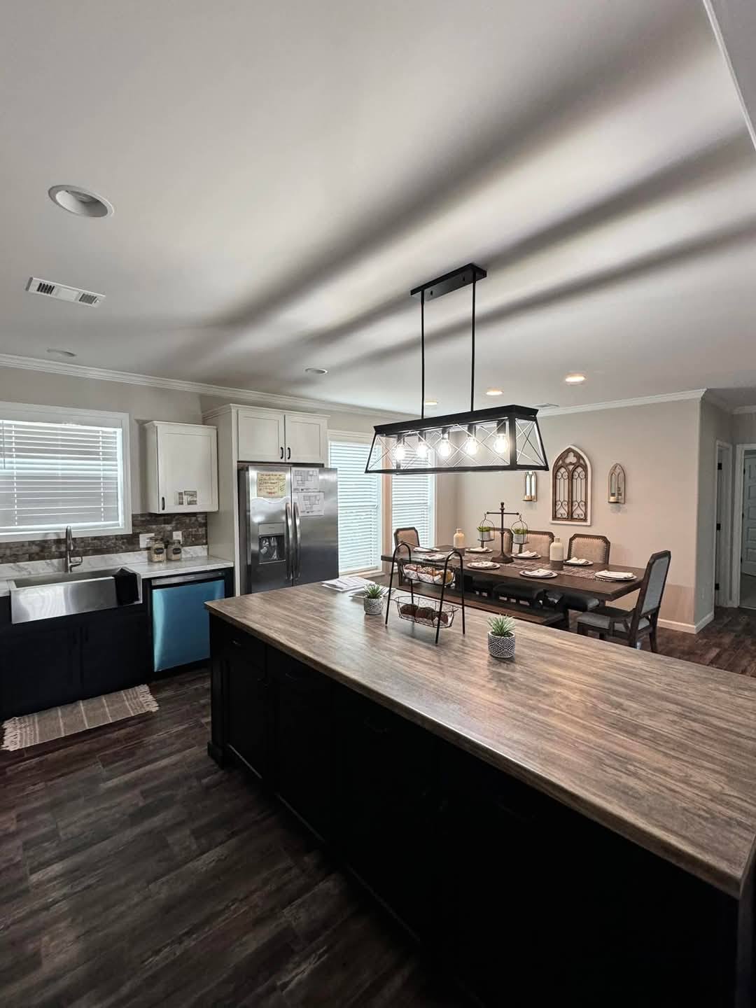 Modern kitchen with a dark wood island, pendant lighting, and farmhouse sink. Dining table set for six, creating a cozy, welcoming atmosphere.
