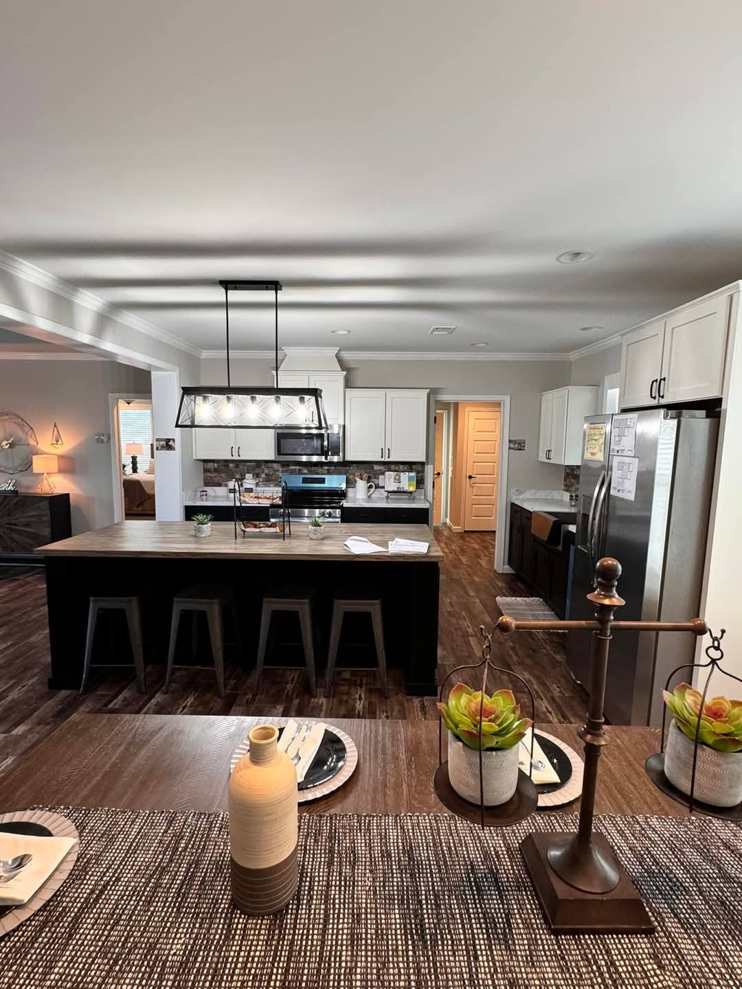 Spacious modern kitchen with dark wood flooring, center island with black stools, stainless steel appliances, and white cabinets. Cozy, inviting atmosphere.