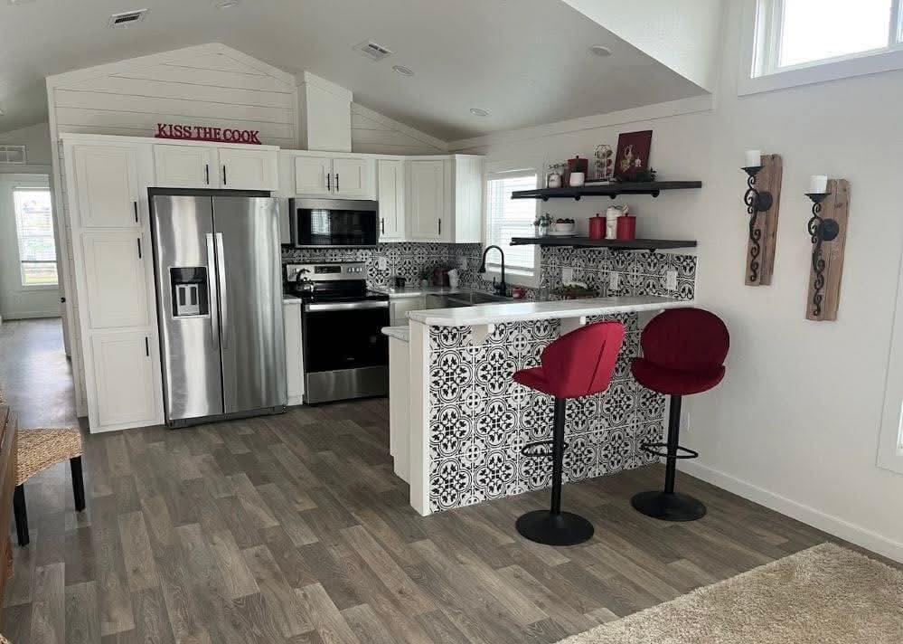 Modern kitchen with a black and white patterned backsplash, stainless steel appliances, and red bar stools. Warm ambiance with wooden and metal accents.