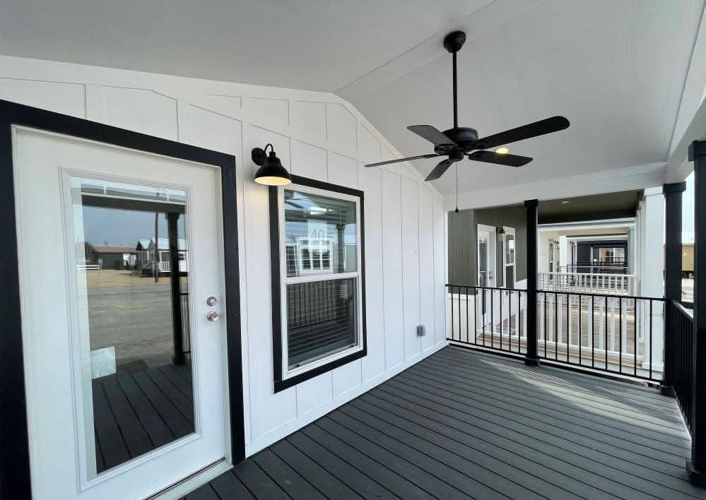 Covered porch with white siding, black trim, and a glass door. A black ceiling fan and light fixture add elegance. Calm and inviting atmosphere.