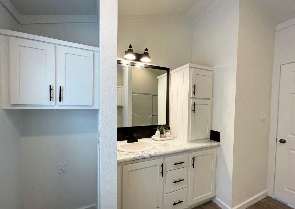 A modern bathroom features white cabinetry with black handles, a large mirror, dual lights, and a marble countertop, creating a fresh, clean ambiance.