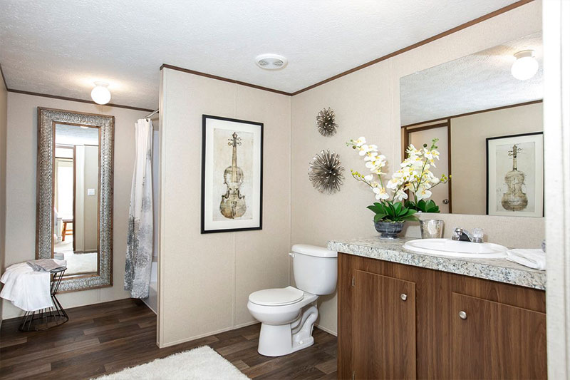 Modern bathroom with wooden cabinets, granite countertop, and white toilet. A flower vase, starburst decorations, and framed violin artwork add elegance.
