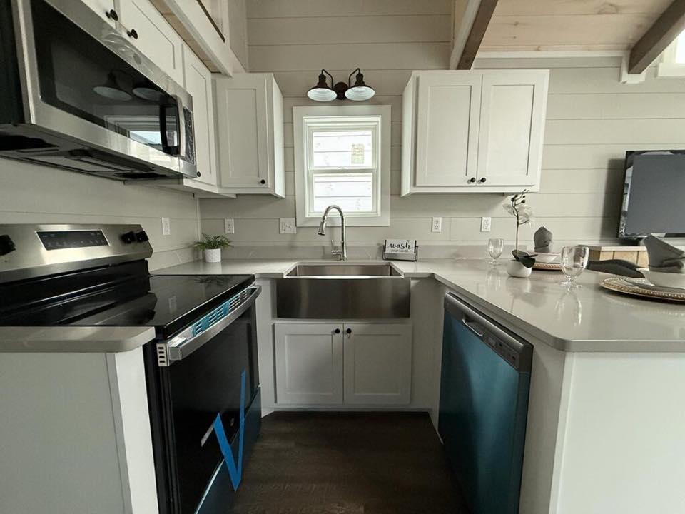 Modern kitchen with white cabinets, stainless steel appliances, and a farmhouse sink. Natural light through a small window creates a cozy feel.
