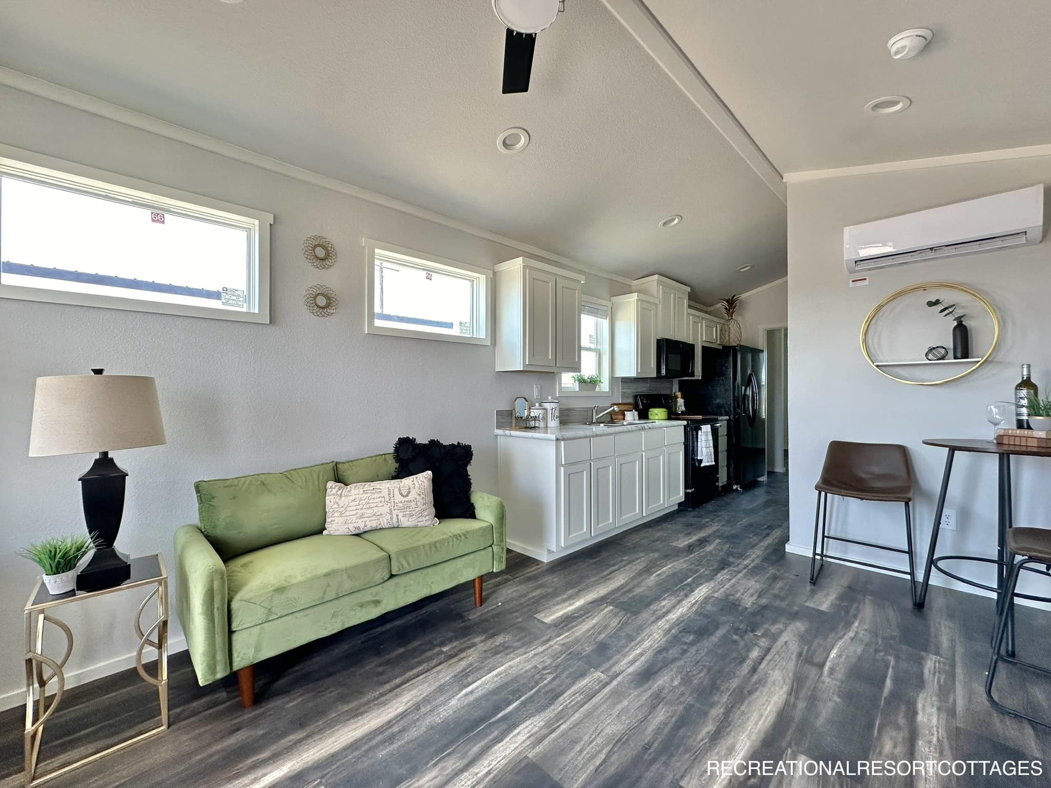 Interior of a modern tiny home with a cozy green sofa, stylish kitchen, and high ceiling. The space feels airy and inviting with natural light.