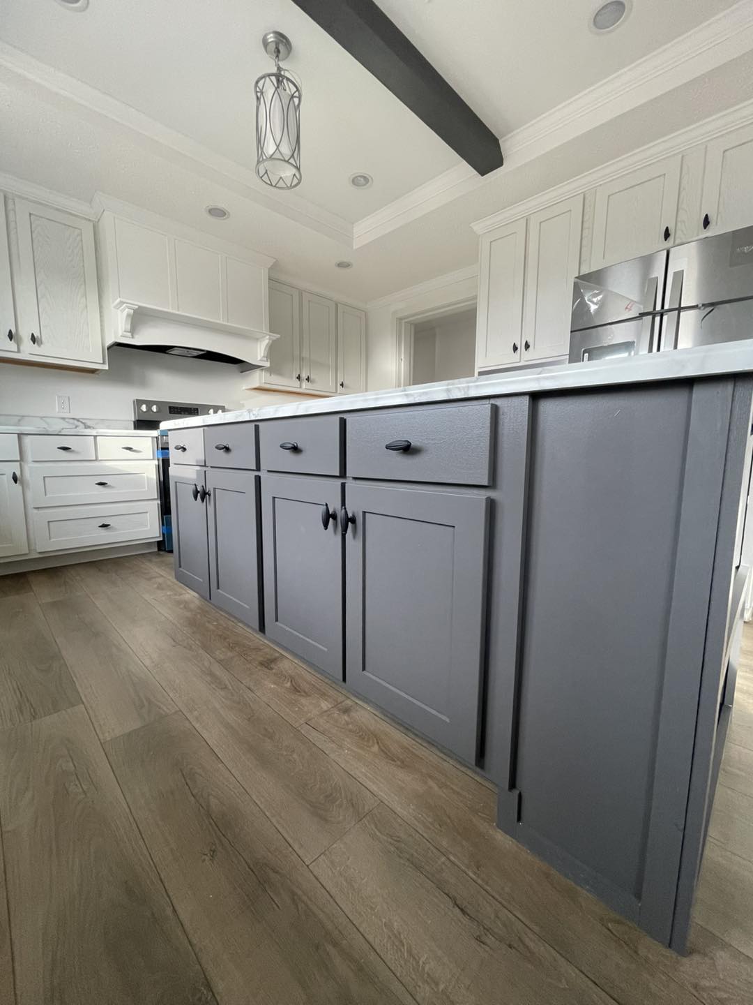 Spacious kitchen with a large gray island, white cabinets, and stainless steel appliances. The wooden floor adds warmth to the modern decor.