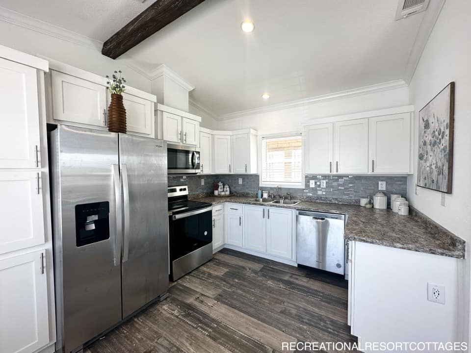 Modern kitchen with white cabinets, stainless steel appliances, and gray tile backsplash. Marble countertops and wood flooring add warmth. Bright, clean ambiance.