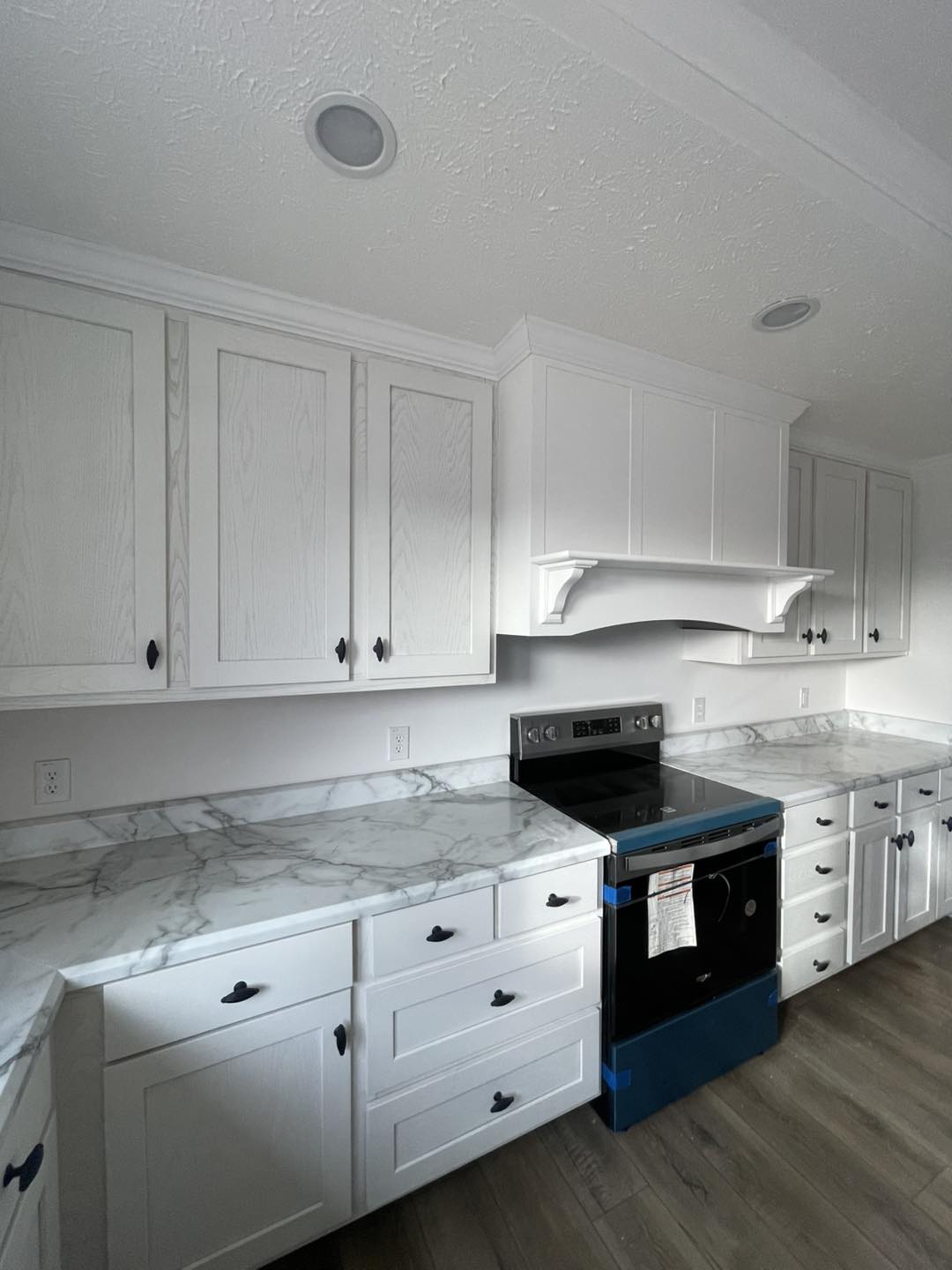 Modern kitchen with white cabinets, marble countertops, and a new stainless steel stove with blue protective film. Bright and clean ambiance.