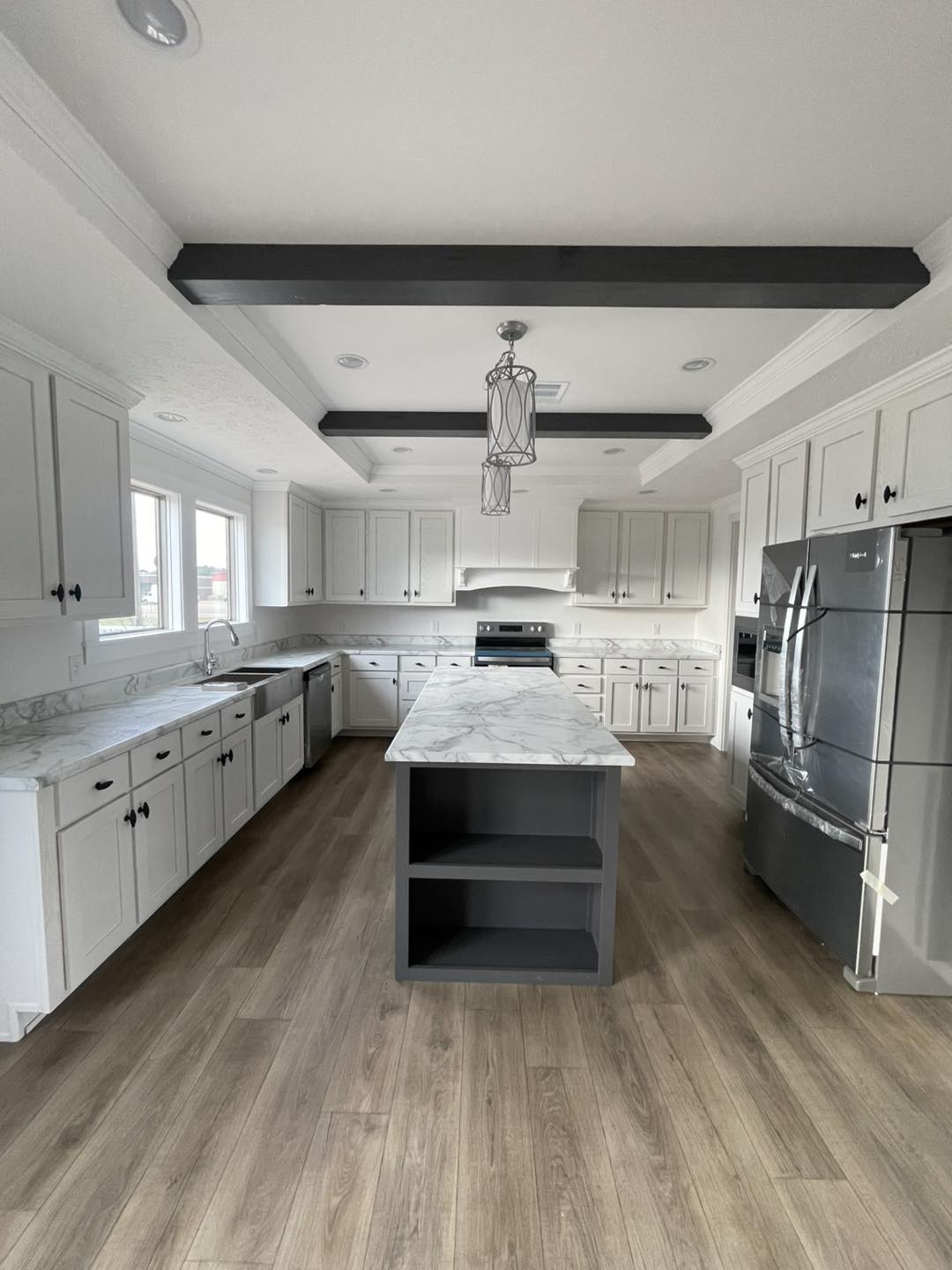 Modern kitchen with light wood floors features a central island with marble countertop, white cabinetry, stainless steel appliances, and large windows.