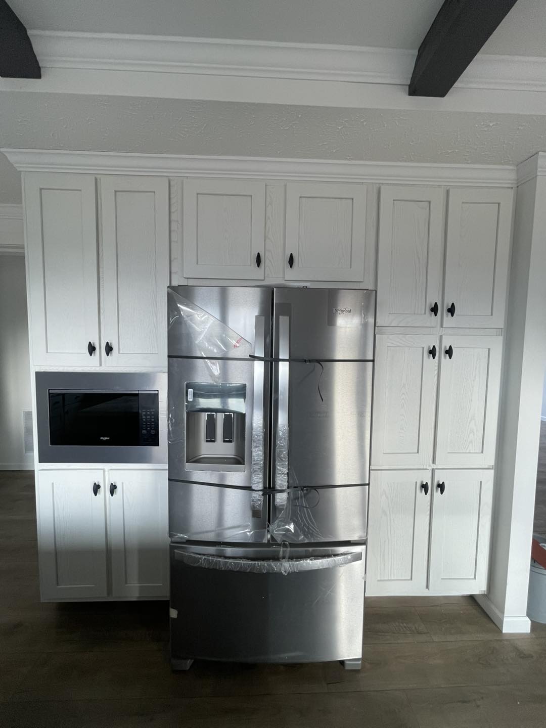 A sleek stainless steel refrigerator with a water dispenser stands amidst white cabinetry. A microwave is built into the cabinet beside it.