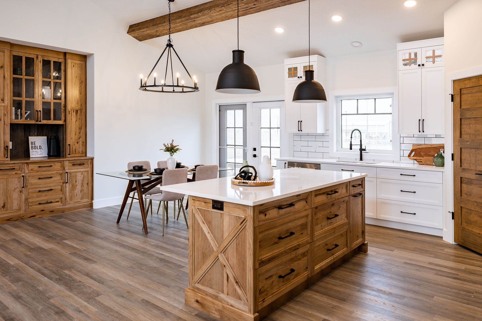 Spacious kitchen with rustic charm features a large wooden island, black pendant lights, white cabinets, and a dining area with glass table and chairs.