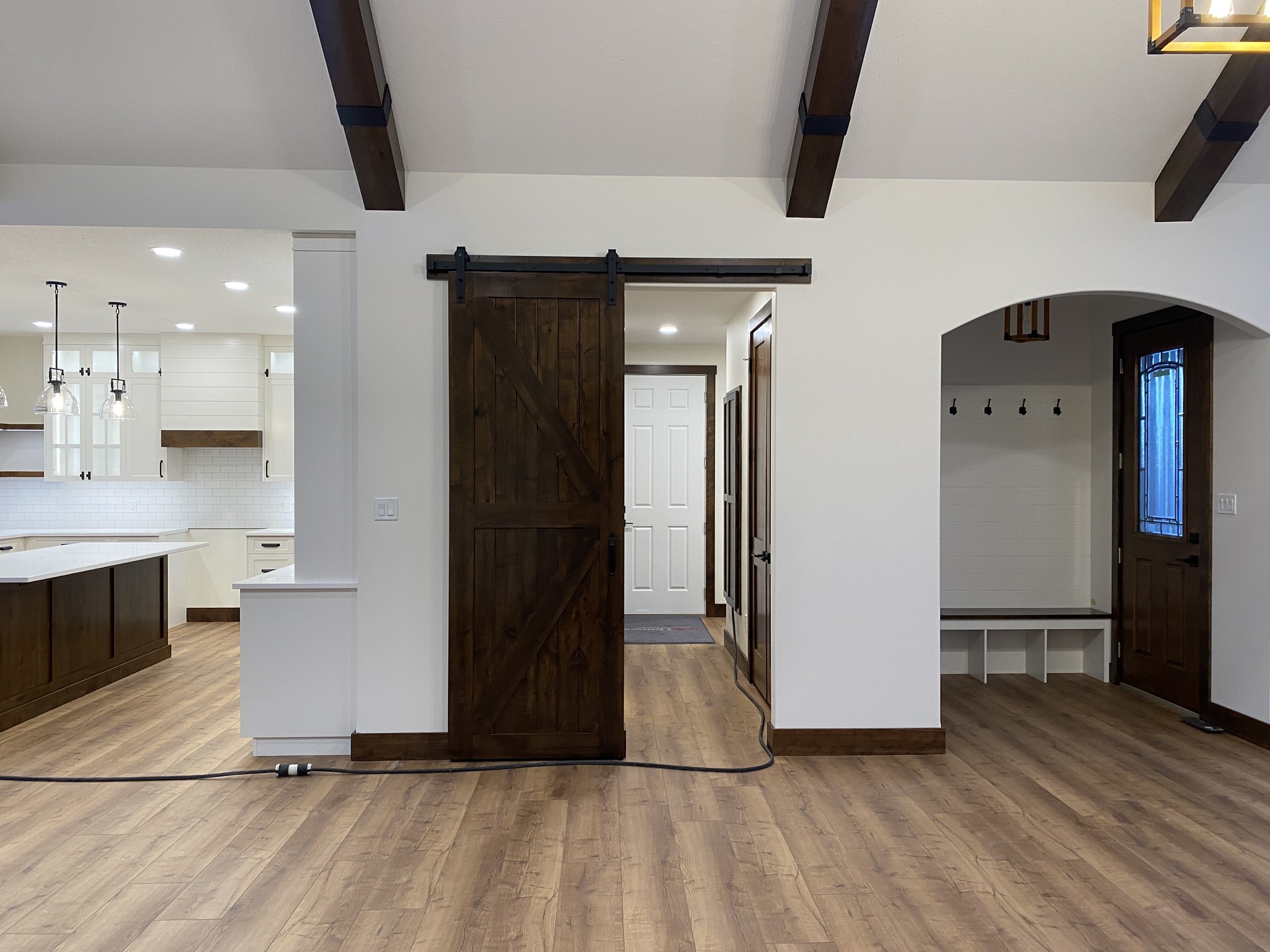 Spacious room with dark wood sliding barn door, white walls, and hardwood floors. Kitchen to the left, entry nook with hooks to the right. Cozy and inviting.