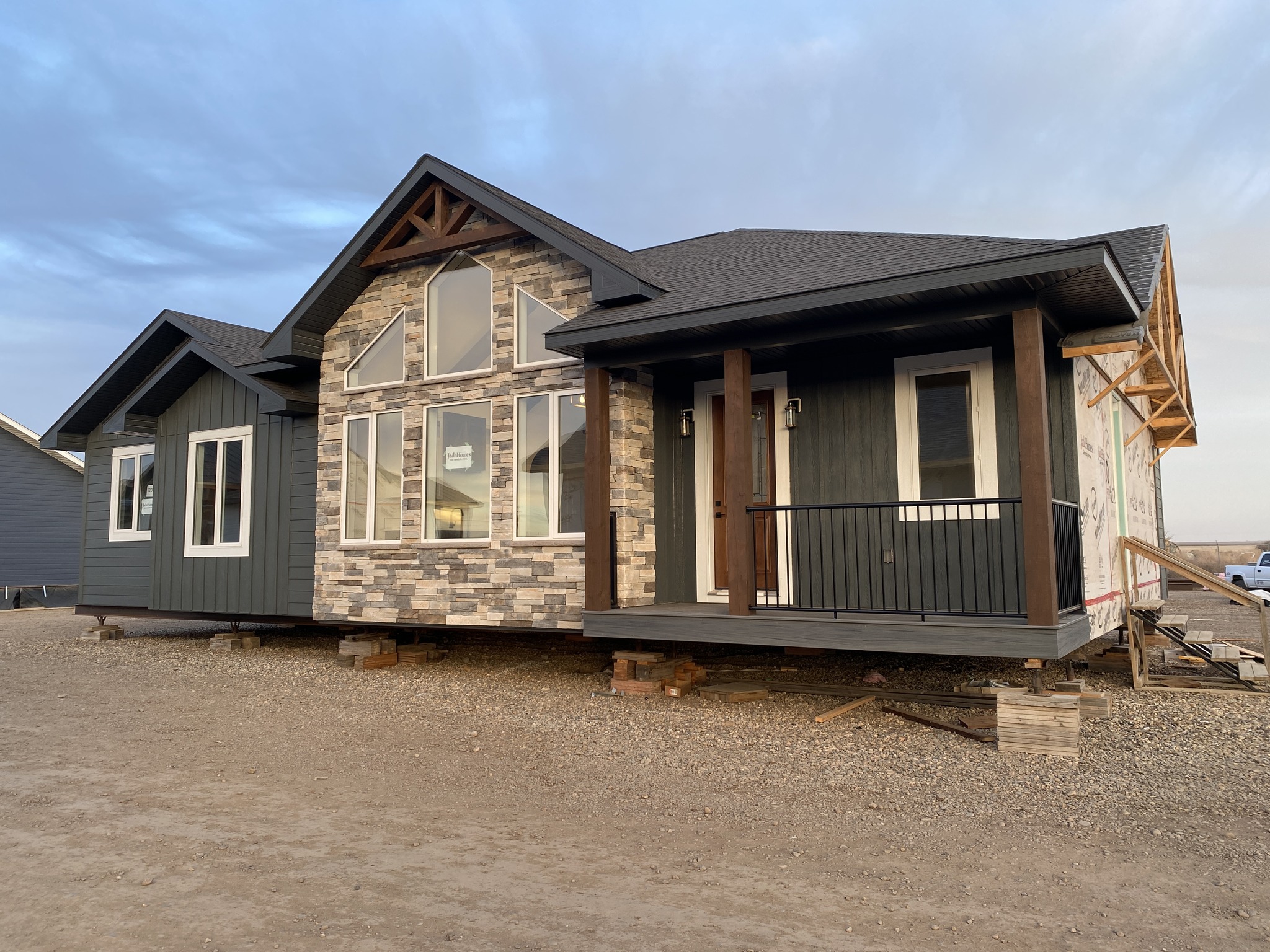 A newly constructed modern house with a mix of dark siding and stone veneer. Large windows and a small front porch create a welcoming appearance.
