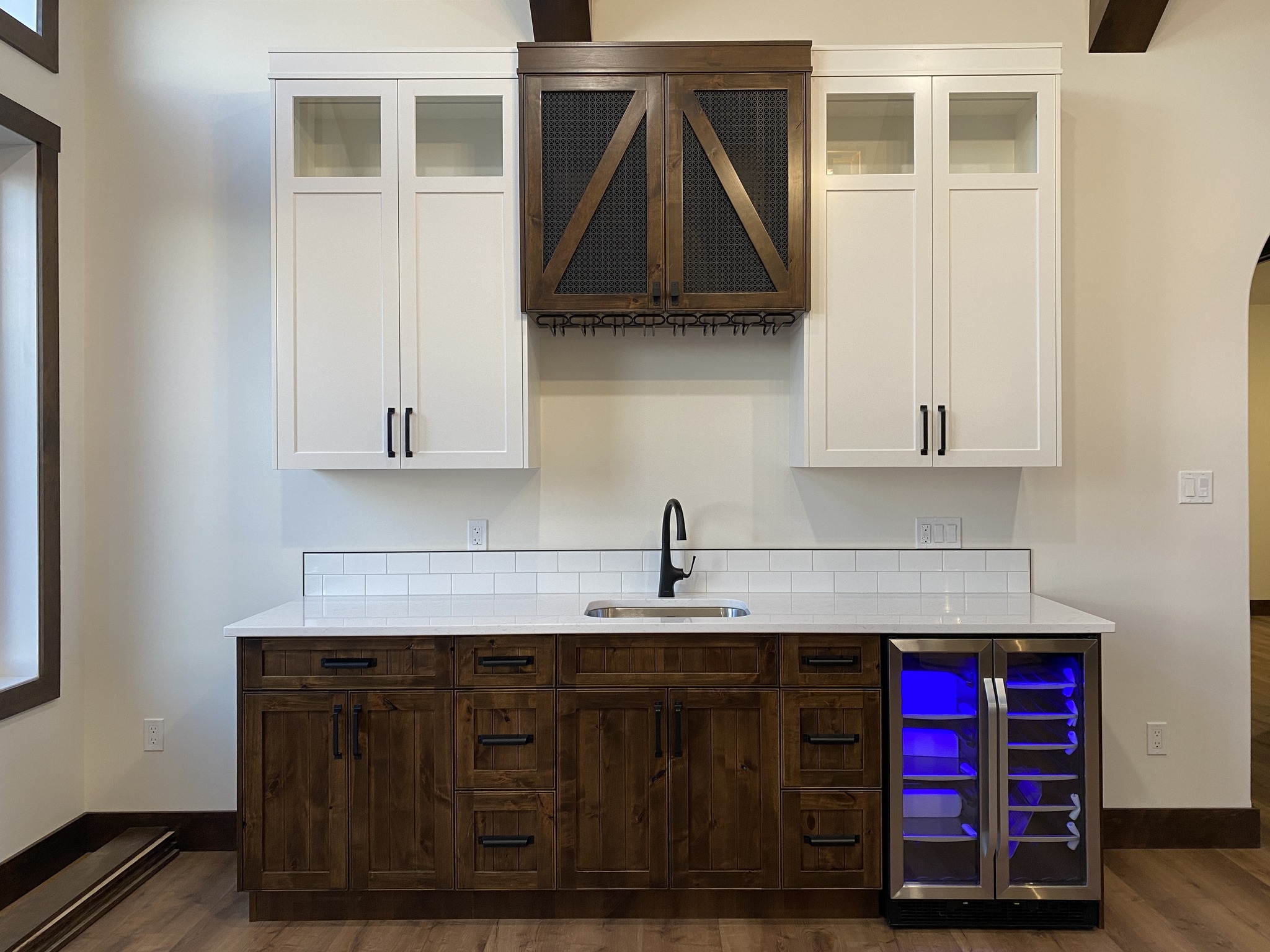 A modern kitchen with a white countertop, dark wood cabinets, a small sink, and a wine cooler with blue lighting. White upper cabinets provide contrast.
