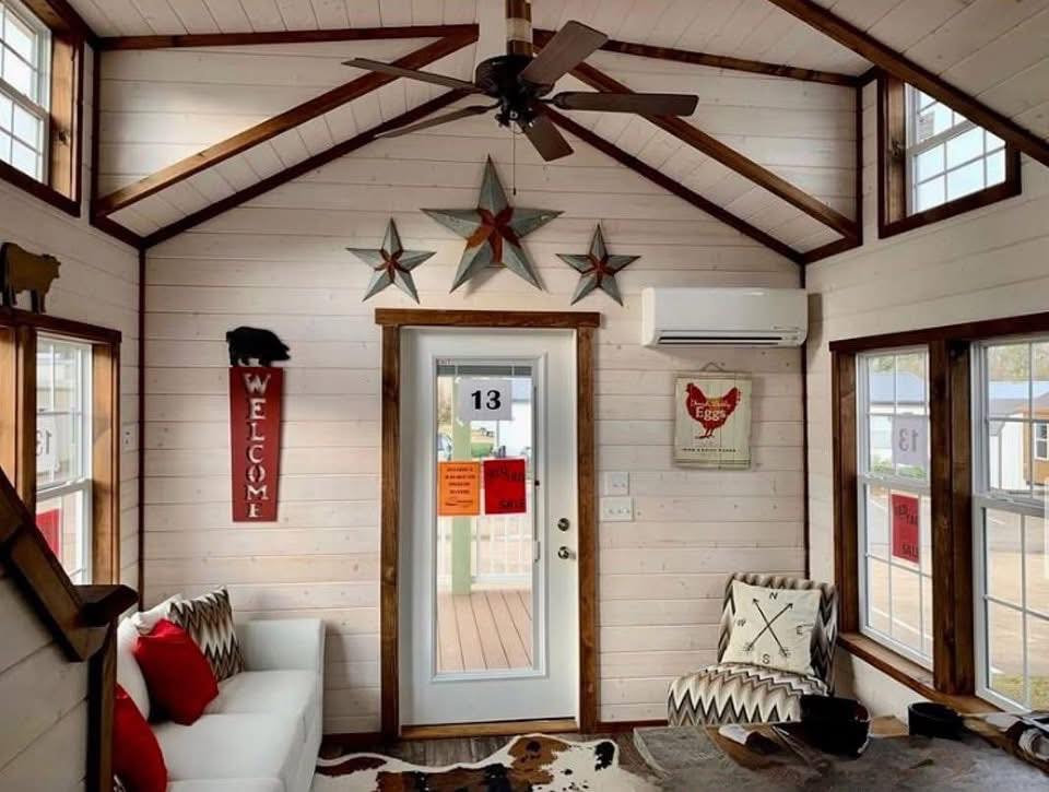 Rustic living room with wood-paneled walls and ceiling, decorated with star ornaments. Cozy white sofa, red pillows, and patterned armchair add charm.