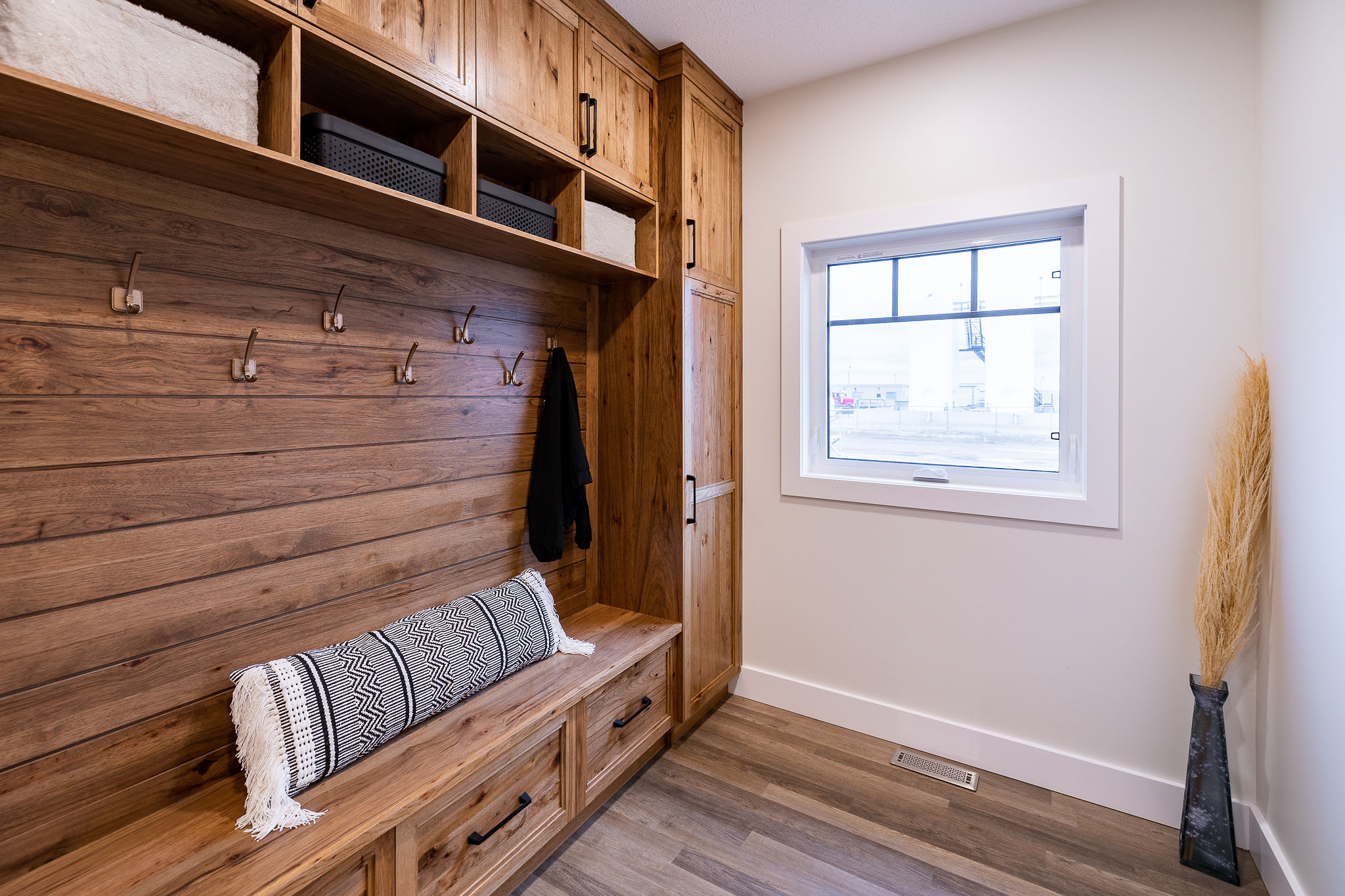 Cozy mudroom with wooden cabinetry and hooks, a bench with a patterned cushion, and a window. Neutral tones convey warmth and simplicity.