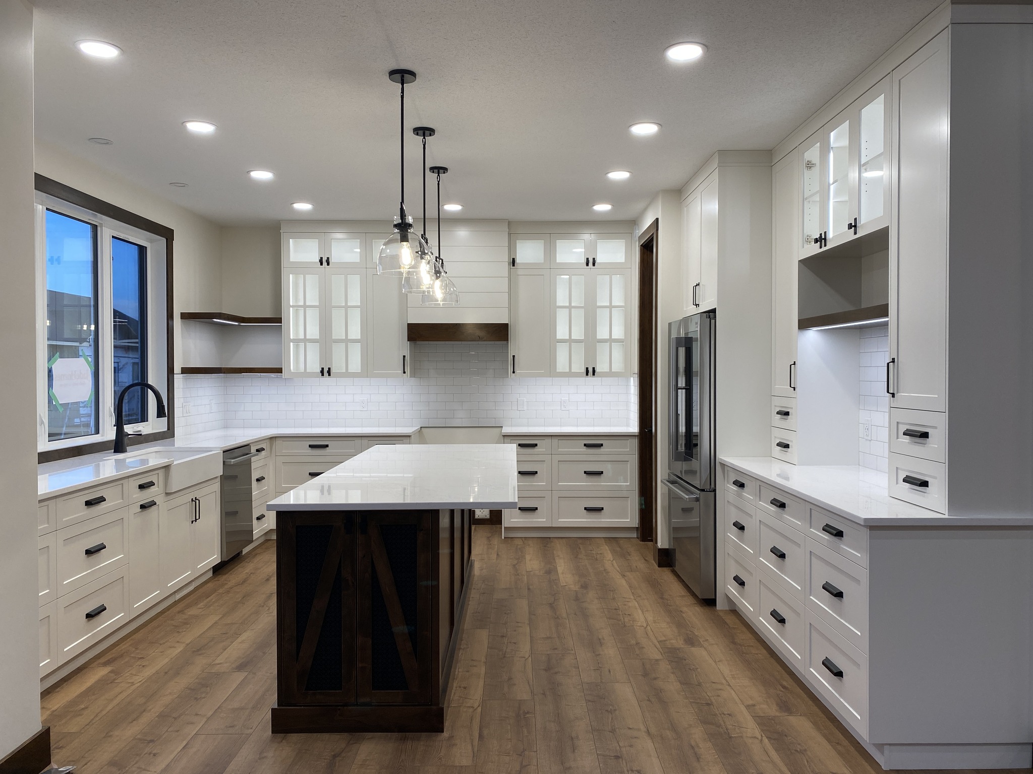 Spacious modern kitchen with white cabinets, wooden floors, a large island with pendant lights, and stainless steel appliances. Bright and inviting atmosphere.