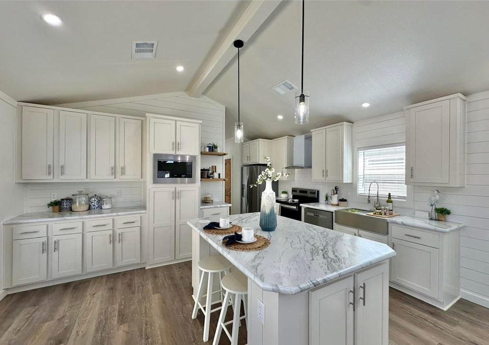 Bright kitchen with white cabinets, marble countertops, and shiplap walls. Center island features stools and stylish pendant lighting. Elegant, airy feel.