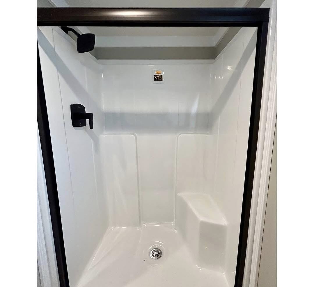 A sleek, modern shower stall with white walls and a seat. It features a black showerhead and fixtures, with a glass door, creating a minimalist, clean look.