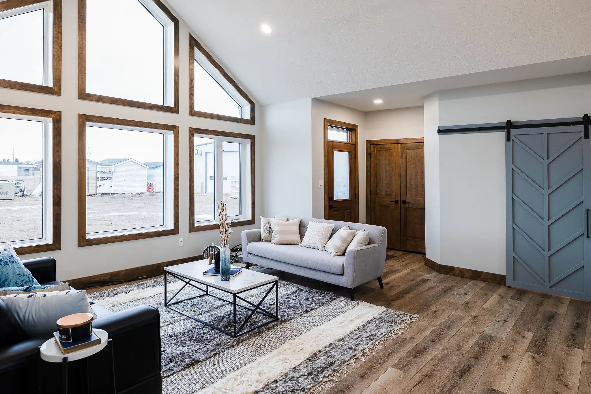 Bright living room with large geometric windows, gray couch, black armchair, and a modern farmhouse sliding barn door. Wood floors add warmth.