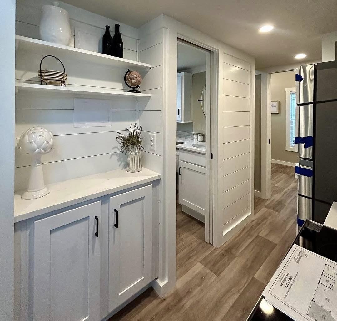 Bright, cozy kitchen nook with white cabinets and shiplap walls. Decor includes vases, books, and globe. Natural wood flooring adds warmth.