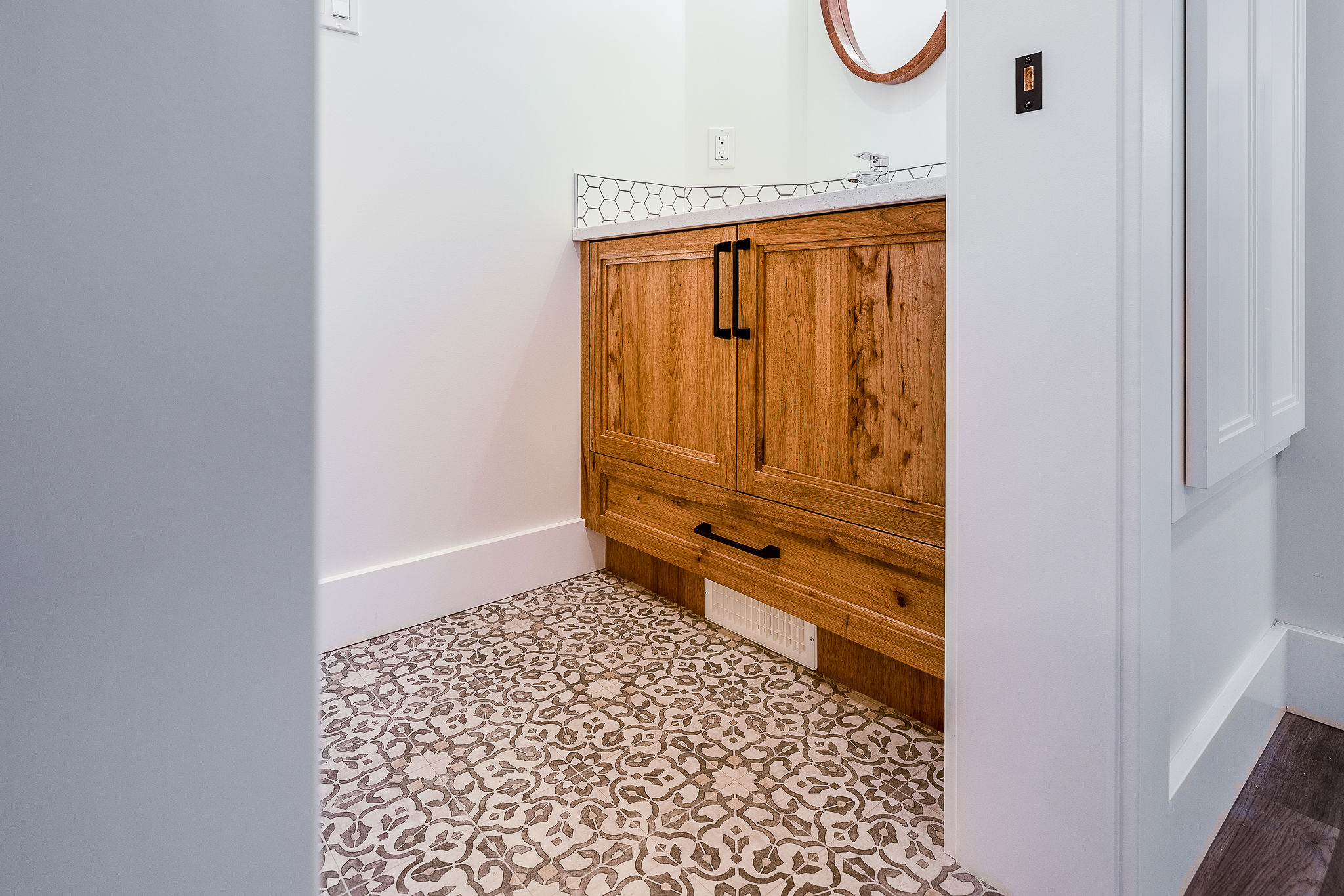Elegant bathroom with geometric patterned tiles and a wooden vanity. The white walls and simple decor create a clean, modern feel.