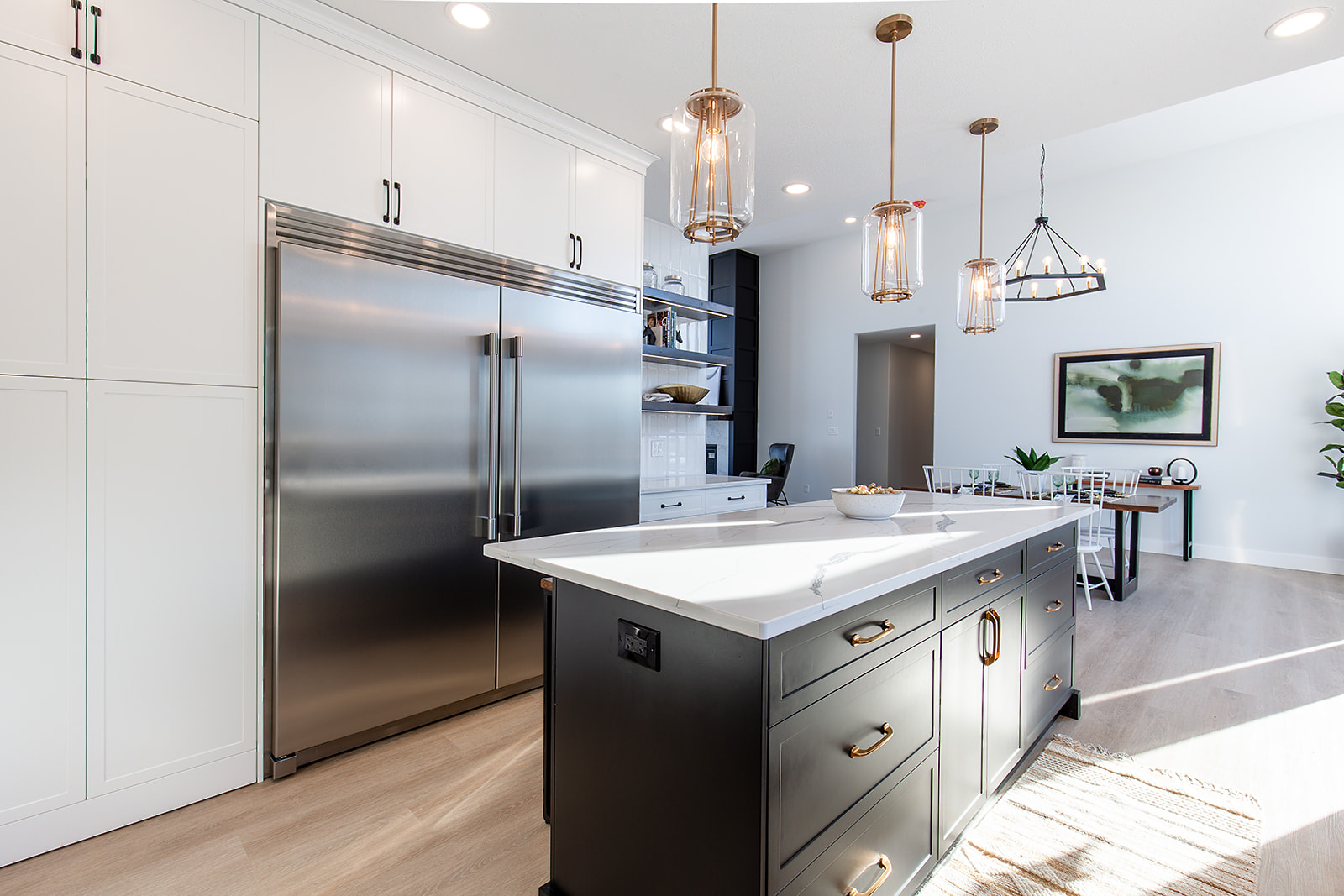 Modern kitchen with a large stainless steel fridge and a sleek island with dark cabinets. Pendant lights hang above the island. Bright and inviting.